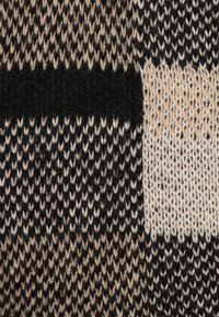 Dzianina z wzorem w kratę w kolorach czarnym, beżowym i kremowym. Tekstura jest miękka, o zróżnicowanym wyglądzie włóczki i wyraźnych blokach kolorystycznych.