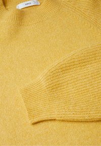 Miękki, żółty sweter z dzianiny z prążkowanymi mankietami i okrągłym dekoltem, ułożony płasko, aby pokazać fakturę i szczegóły materiału.