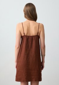Braunes Leinen-Sommerkleid mit dünnen verstellbaren Trägern, das eine lockere Passform und eine glatte Textur aufweist und bis zur Mitte des Oberschenkels fällt.