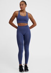 Blå sport-bh och leggings-set gjort av elastiskt tyg, med texturerade mönster och logotypdetaljer, tillsammans med svarta träningsskor.