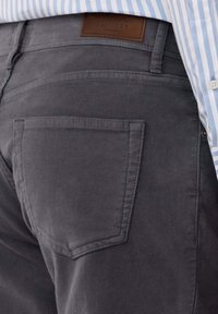Pantalones de algodón gris con un parche de marca de piel etiquetado "Hackett London" sobre un bolsillo trasero, que presentan una textura suave y un diseño ajustado.