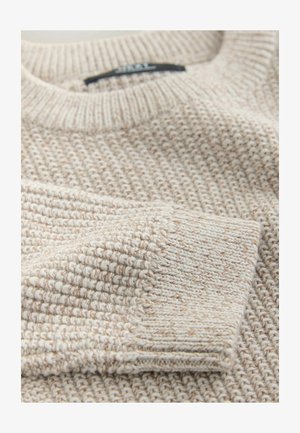 Megztinis iš šviesiai smėlinės spalvos su struktūriniu raštu. Turi ribbėmis apvertą apvalų kaklo iškirpimą ir rankogalius, pabrėždami minkštą, jaukų audinį.