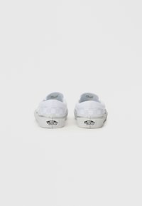 Białe slip-on buty w szachownicę z płaską gumową podeszwą i widocznym logo na pięcie. Gładka tekstylna cholewka z wyściełanym kołnierzem.