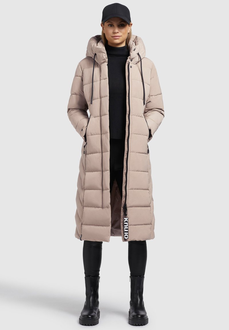 Beige gepolsterter langer Mantel mit Kapuze, mit einem Reißverschluss vorne, Seitentaschen und kontrastierenden Markenlogo-Details entlang des Reißverschlusses.