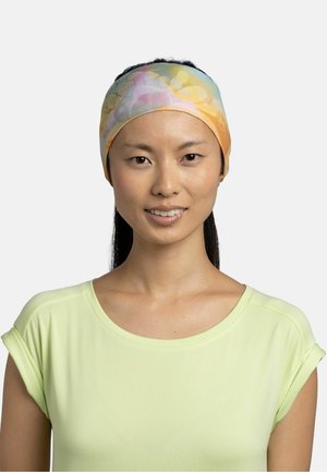 Mujer joven con una diadema multicolor en tonos pastel y una camiseta de manga corta de color amarillo claro, mirando hacia adelante con una ligera sonrisa.
