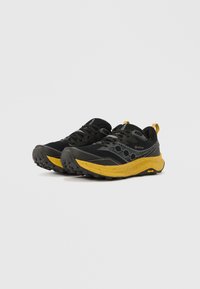Ténis de trail running preto e amarelo com parte superior em Gore-Tex, sola de borracha texturizada e detalhes decorativos laterais. Leves e duráveis.