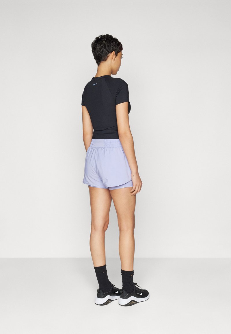 Top ajustado negro de manga corta y pantalones cortos deportivos de color púrpura claro. Tejido ligero, cinturilla elástica, con zapatillas negras y calcetines oscuros.