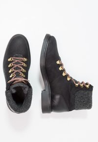 Schwarze Wanderschuhe mit einem Obermaterial aus Wildleder, grauem Stoffkragen, goldenen Beschlägen und rosa-weißen Schnürsenkeln, mit einer robusten Gummisohle.