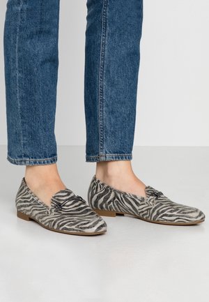 Zebratulpaiset loafertossut, joissa on harmaan ja mustan teksturoitunut materiaali, matala korko ja koristeellinen vyö yläosassa. Yhdistettyinä sinisiin farkkuihin.