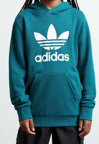 Teal hoodie made of cotton blend, featuring a large white Adidas logo and three stripes. Includes a kangaroo pocket and ribbed cuffs.