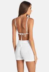 Vitt stickat tvådelat set med en ryggknuten bralette-top och löst sittande shorts, båda i en texturerad tyg med ribbade detaljer.