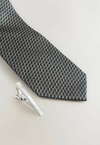 Navyblaues Krawatte mit einem geometrischen Muster in Creme und Blau, kombiniert mit einem eleganten silbernen Krawattenclip mit rechteckigem Design.