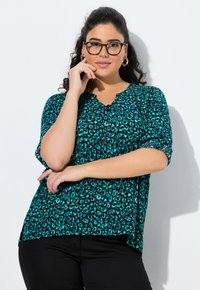Blusa con stampa animale color teal, dotata di scollatura a V, maniche corte arrotolate e orlo curvo. Il tessuto sembra leggero e presenta una consistenza liscia.