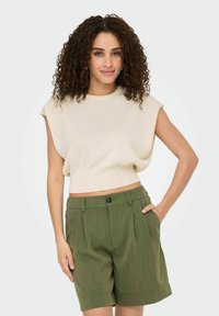 Cremfarbener, kurzärmeliger, kurzer Stricktop kombiniert mit olivgrünen, gefalteten, knielangen Shorts mit Seitentaschen und Knopfverschluss.