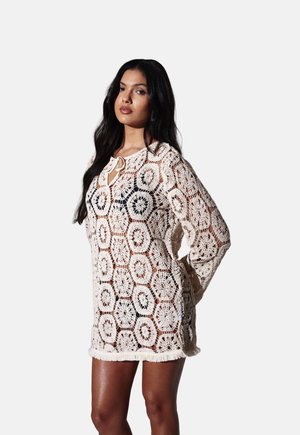 Hæklet cover-up i creme; sekskantet mønster med åben vævning og frynsekant. Har bindelukning i halsudskæringen. Lange ærmer.