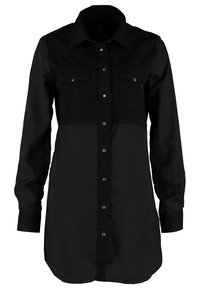 Camisetta nera a maniche lunghe con chiusura a bottoni sul davanti, due tasche sul petto e tessuti di trama contrastante nelle sezioni superiore e inferiore.