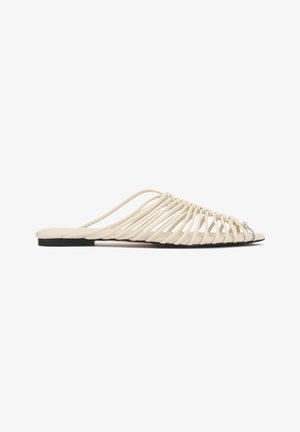 Flat slide sandal with multiple thin cream-colored straps forming an open cage design and a black sole.