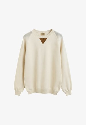 Maglione lavorato a maglia color crema con maniche lunghe, polsini e orlo a costine, e una piccola toppa triangolare marrone sotto la scollatura.