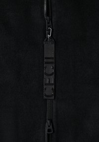 Gros plan d'une fermeture éclair noire sur un tissu noir avec une languette noire affichant des lettres en relief "CECIL".