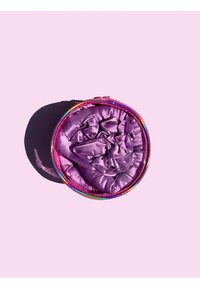 Chouchou en satin violet rangé dans un contenant rond zippé avec un accent arc-en-ciel sur le couvercle, sur un fond rose.