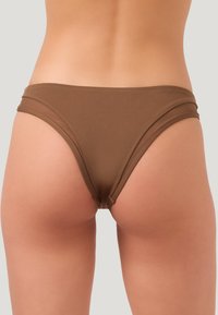 Bas de bikini marron avec un design sans coutures, une couverture modérée et un tissu doux et texturé. Présente des découpes sur les côtés pour un look élégant.