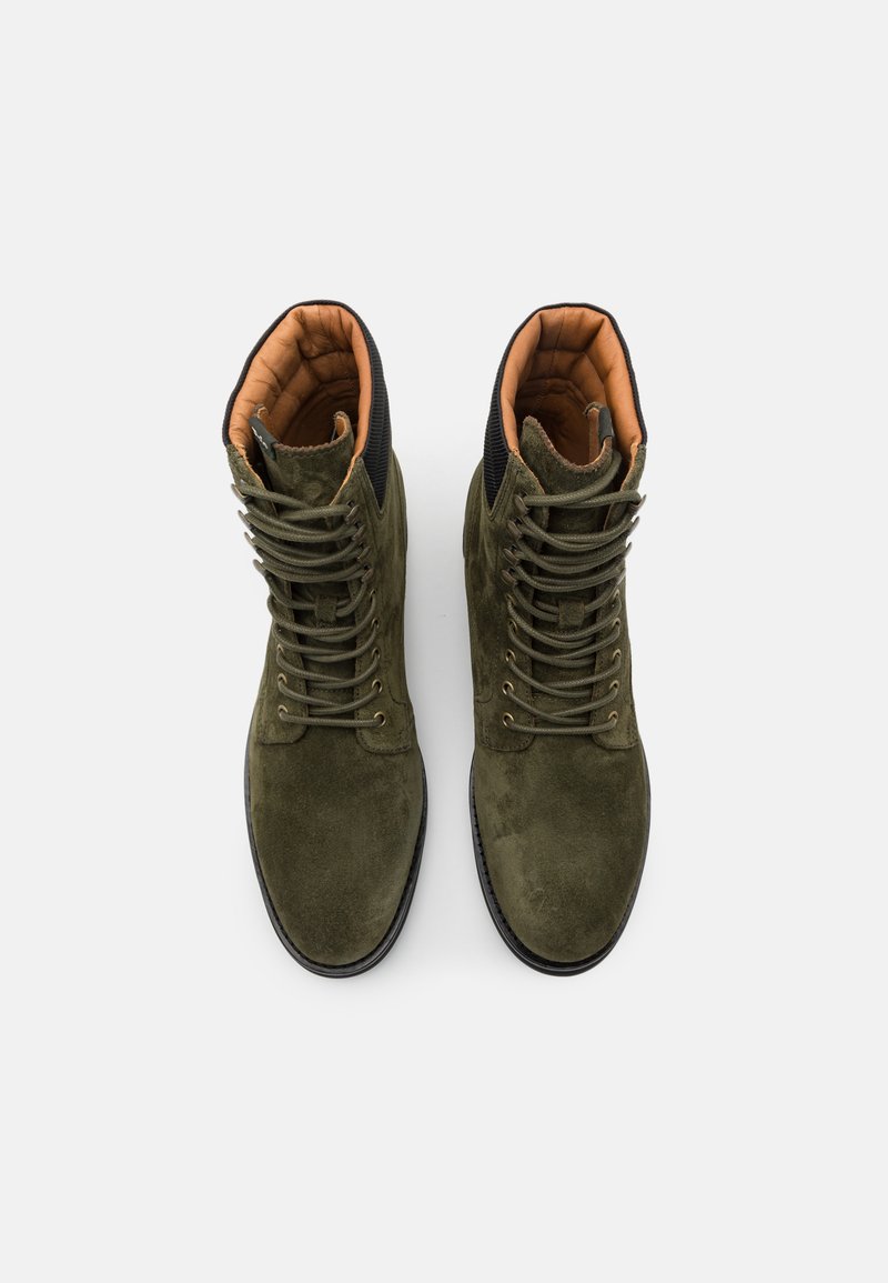 Olivgrüne Wildlederstiefel mit einem gepolsterten braunen Innenleben, schwarzen Akzenten und Schnürung mit sechs Ösen, ausgestattet mit einer runden Zehenpartie und einer flachen Sohle.