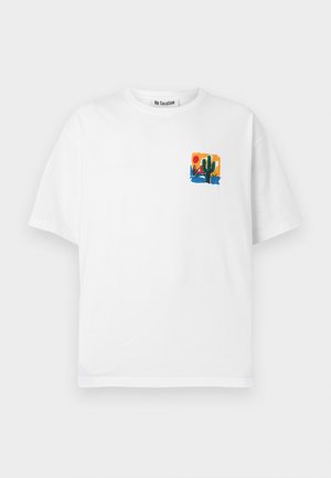 Biele tričko s krátkym rukávom s malou farebnou grafikou púšte zobrazujúcou kaktus, západ slnka a rastliny v oblasti ľavej hornej časti na hrudi.