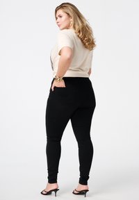 Zwarte skinny jeans met een gladde textuur, achterzakken en een hoge taille, gecombineerd met een lichtbeige t-shirt en hoge sandalen.
