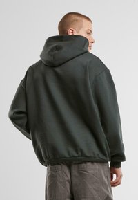 Dark green hoodie featuring a large hood, ribbed cuffs, and hem, shown from the back with a smooth texture and relaxed fit.