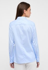 Light blue long-sleeve shirt with a collar, smooth texture, button cuffs, and a back yoke seam. Simple and tailored design.