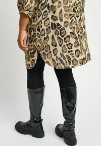 Široka košulja s leopard uzorkom dugih rukava, u kombinaciji sa crnim tajicama i visokim, sjajnim crnim čizmama s debelim đonovima.