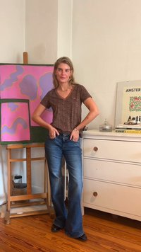 Top de cuello en V de manga corta con estampado animal marrón, jeans acampanados azules, zapatos negros. El fondo presenta una obra de arte abstracta rosa y muebles de colores claros.