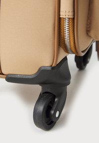 Beige softshell suitcase corner with black plastic support and wheel. Features a metal zipper and tan stitching detail on the edge.