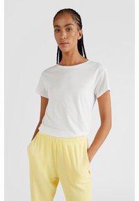 Witte katoenen t-shirt met korte mouwen en een ronde hals, gecombineerd met lichtgele joggingbroek met elastische tailleband en koord.