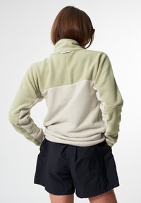 Fleecejacke mit geteilt Design in Hellgrün und Creme, mit hohem Kragen und strukturiertem Stoff. Kombiniert mit schwarzen Shorts.