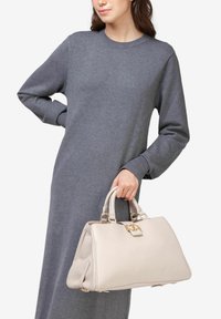 Lys beige håndtaske med tekstureret overflade, guld hardware og to håndtag; båret med en lang grå sweaterkjole.