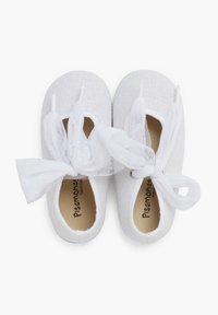 Zapatos de tela blanca con una superficie texturizada, presentan lazos de tul blanco translúcido en la parte delantera y un forro interior marrón con la marca.