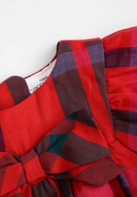 Tkanina w czerwoną i ciemnoniebieską kratę zdobi duża kokarda przy dekolcie. Tekstura jest gładka z lekkim połyskiem.