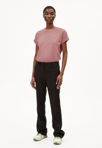 Rosa kurzärmeliges T-Shirt, schwarze maßgeschneiderte Hose und weiße Sneakers mit grünen Akzenten. Einfaches Design, glatter Stoff und eine lässige Passform.