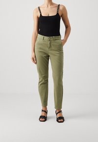 Svart ribbad linne med dekorativa remmar, olivgröna slim-fit byxor och svarta sandaler med remmar. Släta texturer och figurnära siluett.