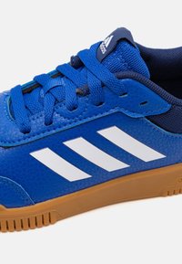 Modré tenisky Adidas s bílými pruhy, modrými tkaničkami a gumovou podrážkou, ukazující texturovanou kůži a síťovinový jazyk.