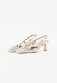 Srebrne buty typu slingback z wąskimi czubkami, teksturowana cholewka z wzorem diamentowym oraz smukłe słupkowe obcasy. Udekorowane metalicznym wykończeniem.