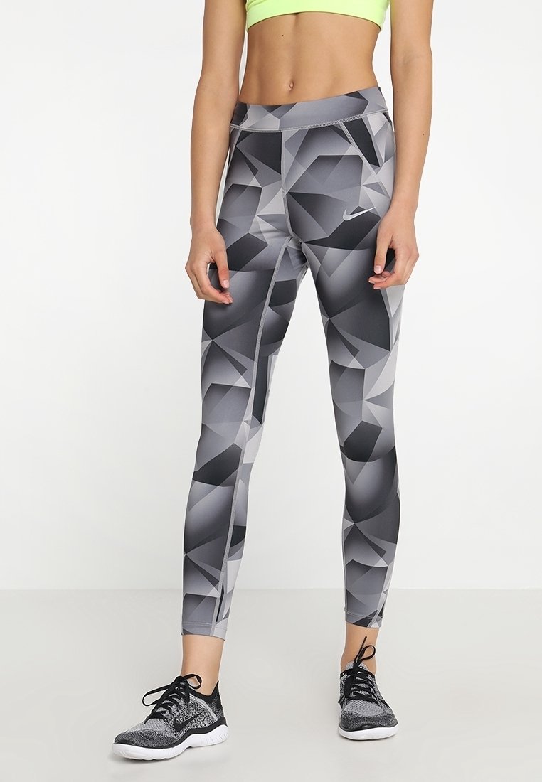 Legíny Nike v geometrickém šedém vzoru, s vysokým pasem a elastickým materiálem. V páru s černými sportovními botami.