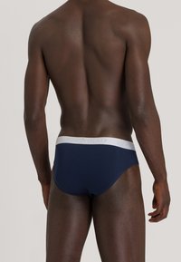 Slip blu navy con un elastico bianco in vita che presenta il logo del marchio. Texture liscia, vestibilità aderente e design classico.