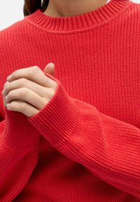 Suéter rojo de punto con cuello y puños acanalados. La textura es suave y elástica, con mangas largas y un ajuste relajado.