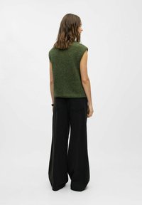 Haut sans manches en tricot vert avec une finition texturée, associé à un pantalon noir large avec des poches à l'arrière et une coupe décontractée.