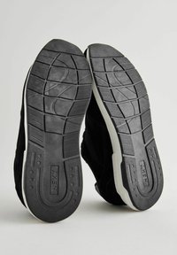 Schwarze Wildleder-Sneaker-Sohle mit einem strukturierten Gummimuster, das eine kontrastierende weiße Kante und ein Branding an der Ferse aufweist.