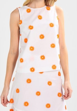 Bez rękawów biały komplet top i spódnica z jaskrawym pomarańczowym wzorem kwiatowym noszony przez stojącą osobę na jednolitym tle.