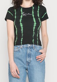 Black cotton t-shirt with green tie-dye stripes, featuring a white cursive logo. Fitted design with short sleeves and a cropped length.