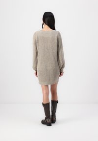 Beige stickad klänning med en figurnära silhuett, långa puffärmar och ribbat halsband. Svarta knähöga stövlar med spännen.